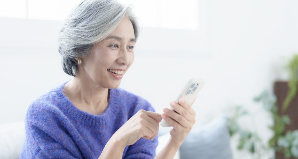 自宅でスマホを見て笑顔のシニア女性