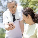 ウォーキングの休憩中にスマホを観て笑顔のシニア夫婦