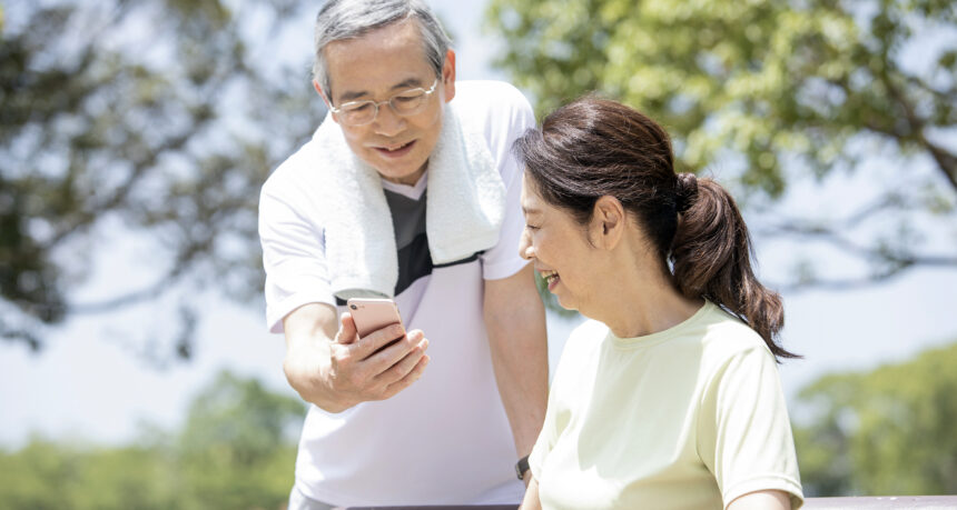 ウォーキングの休憩中にスマホを観て笑顔のシニア夫婦