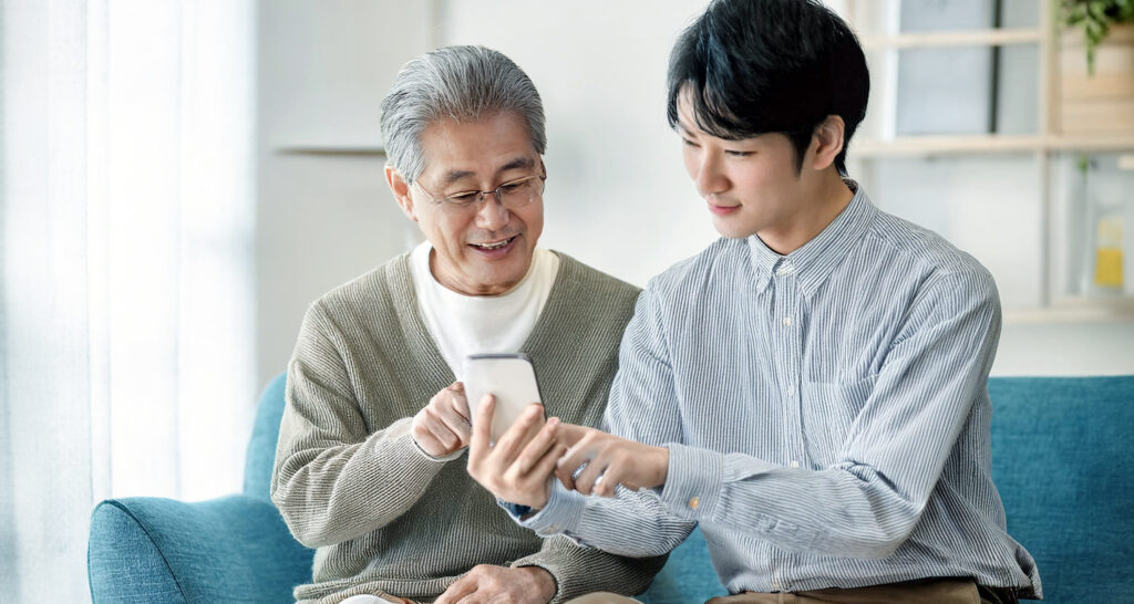孫にスマホのことを教えてもらうシニア男性