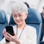 飛行機の中でスマートフォンを操作するシニア女性