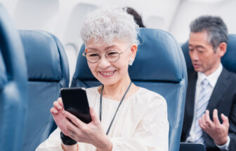飛行機の中でスマートフォンを操作するシニア女性