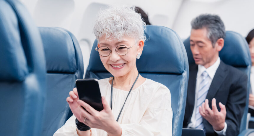 飛行機の中でスマートフォンを操作するシニア女性