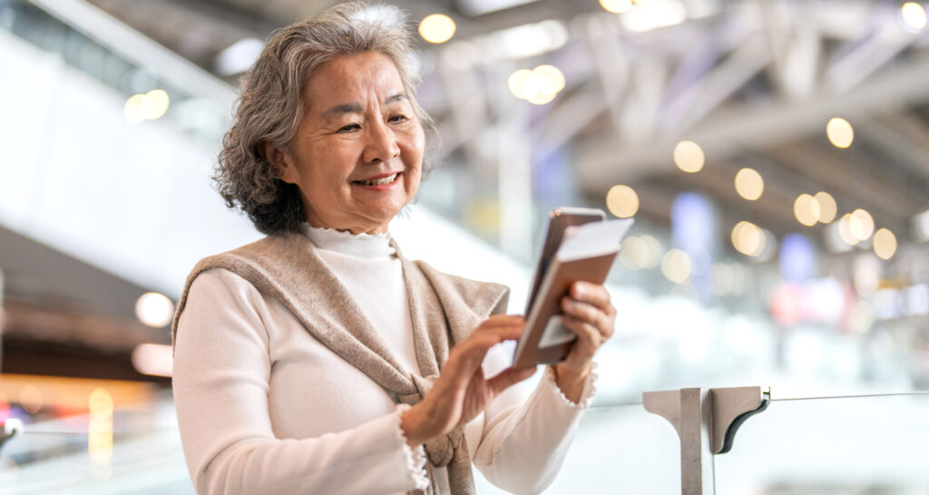 空港でスマートフォンを操作するシニア女性