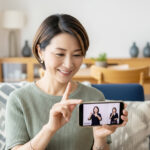 おしゃれな自宅でスマートフォンで動画を見ながら手話を学ぶ笑顔の日本人ミドル女性
