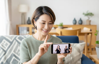 おしゃれな自宅でスマートフォンで動画を見ながら手話を学ぶ笑顔の日本人ミドル女性