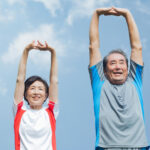 青空の下でラジオ体操をするシニア夫婦