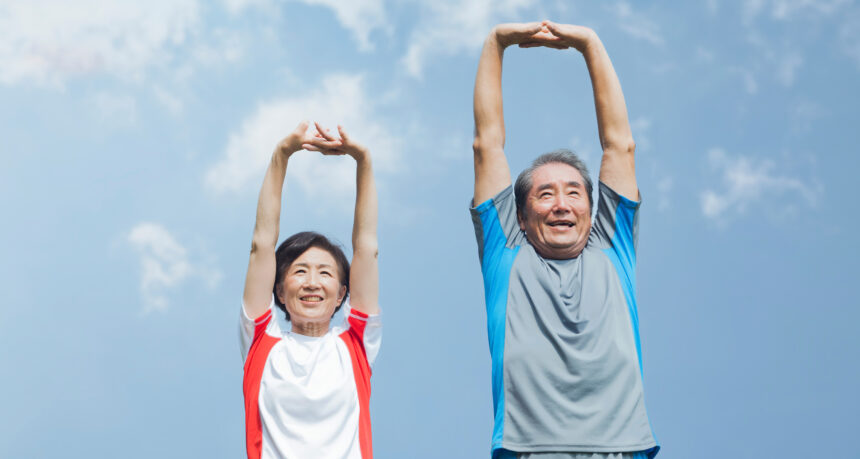 青空の下でラジオ体操をするシニア夫婦