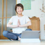 自宅でタブレットを見ながらストレッチをする日本人女性