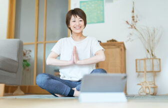 自宅でタブレットを見ながらストレッチをする日本人女性