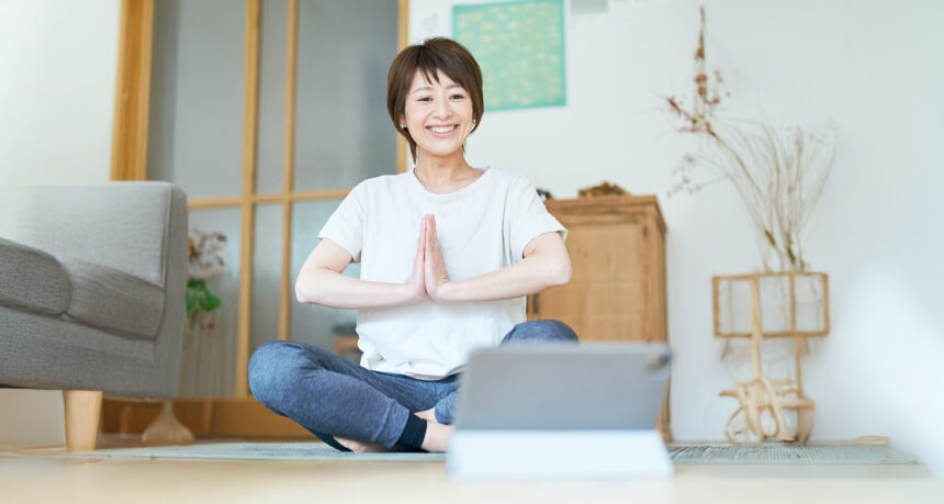 自宅でタブレットを見ながらストレッチをする日本人女性