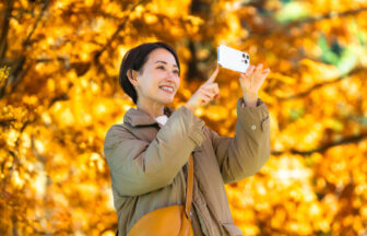 美しい紅葉の写真をスマートフォンで撮影するミドル女性