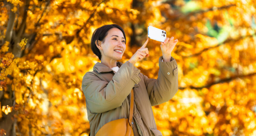 美しい紅葉の写真をスマートフォンで撮影するミドル女性