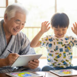 おじいちゃんと孫が笑顔でタブレットで塗り絵をしている