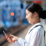 駅のホームでスマートフォンで電車の時間を確認する日本人ミドル女性