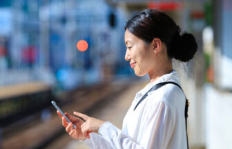 駅のホームでスマートフォンで電車の時間を確認する日本人ミドル女性