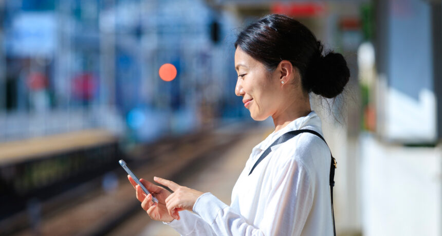 駅のホームでスマートフォンで電車の時間を確認する日本人ミドル女性