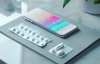 デスクの上にスマートと薬を並べたスマートフォンで薬管理をするイメージ