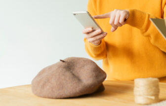 インターネットで手作りの帽子を販売するために帽子をスマートフォンで撮影をしている女性