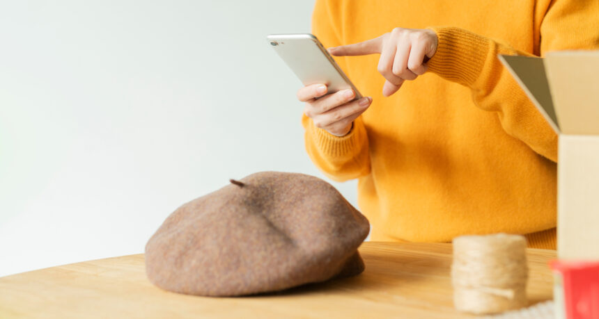 インターネットで手作りの帽子を販売するために帽子をスマートフォンで撮影をしている女性