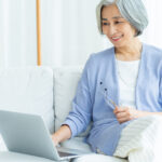 爽やかな日本人シニア女性がソファの上でリラックスしてパソコンでオンライン講座を受けている様子