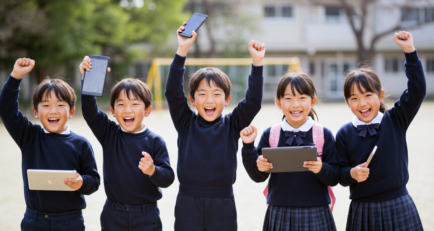 男女５人の子どもたちが横1列に並び、タブレットやスマートフォンを掲げて元気よくガッツポーズをしている