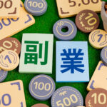 おもちゃのお金と積み木にプリントされた副業の文字