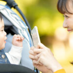 スマートフォンでベビーカーに乗った子どもを撮影するママ