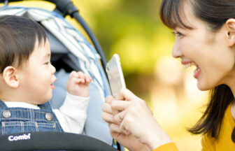 スマートフォンでベビーカーに乗った子どもを撮影するママ