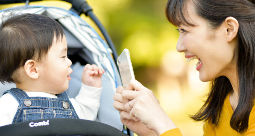 スマートフォンでベビーカーに乗った子どもを撮影するママ